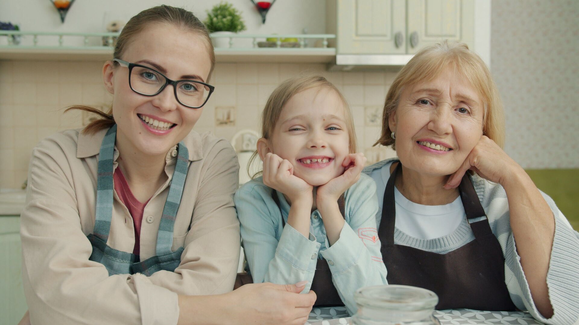 Smiling grandmother, adult daughter and granddaughter leaning together at a kitchen table